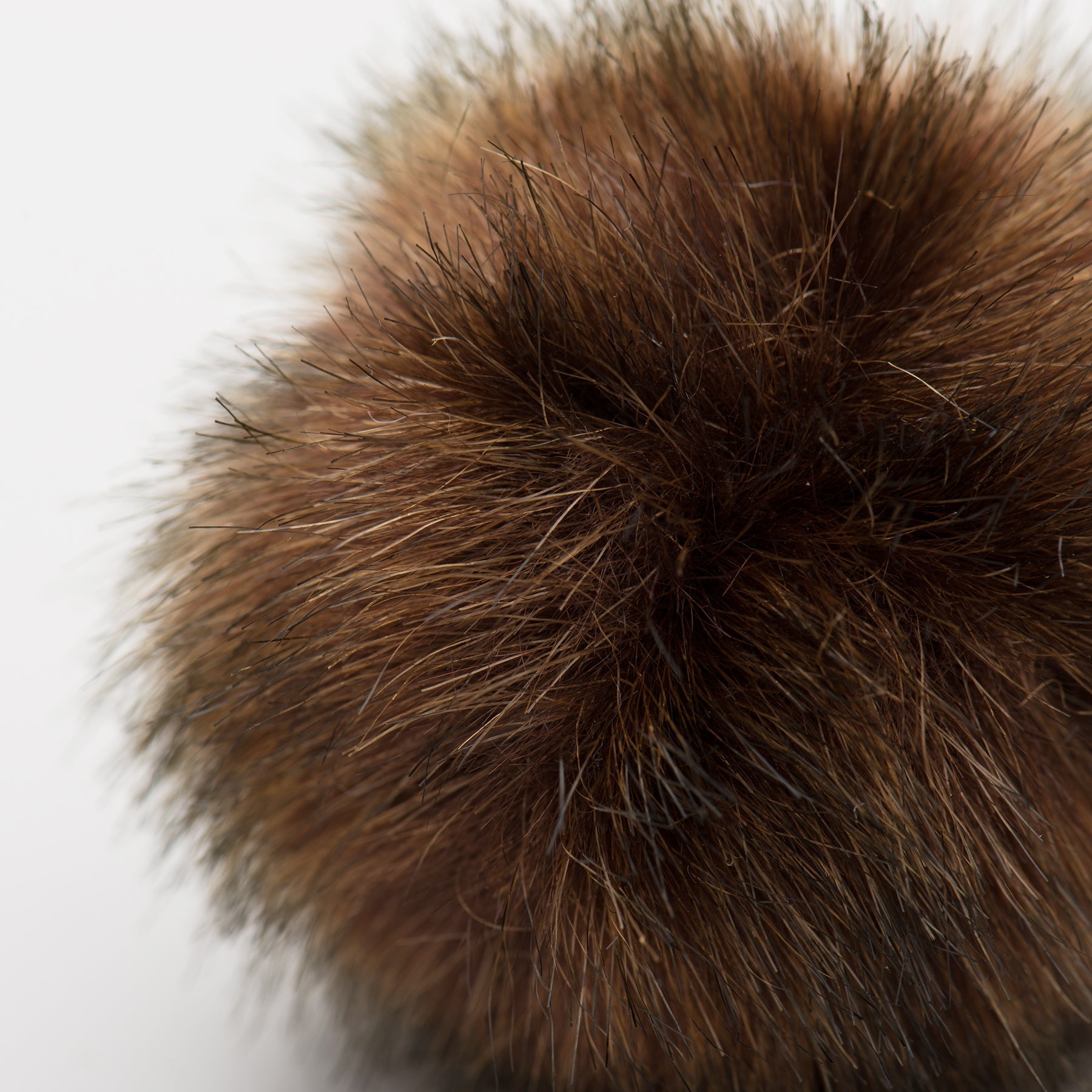 Close-up of a brown fur pom-pom cat toy on a white background.
