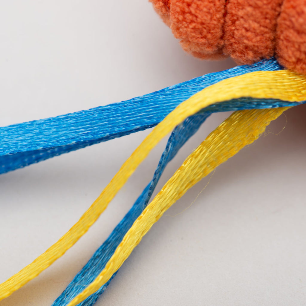 Close-up of blue and yellow ribbons on an orange cat toy in the background.