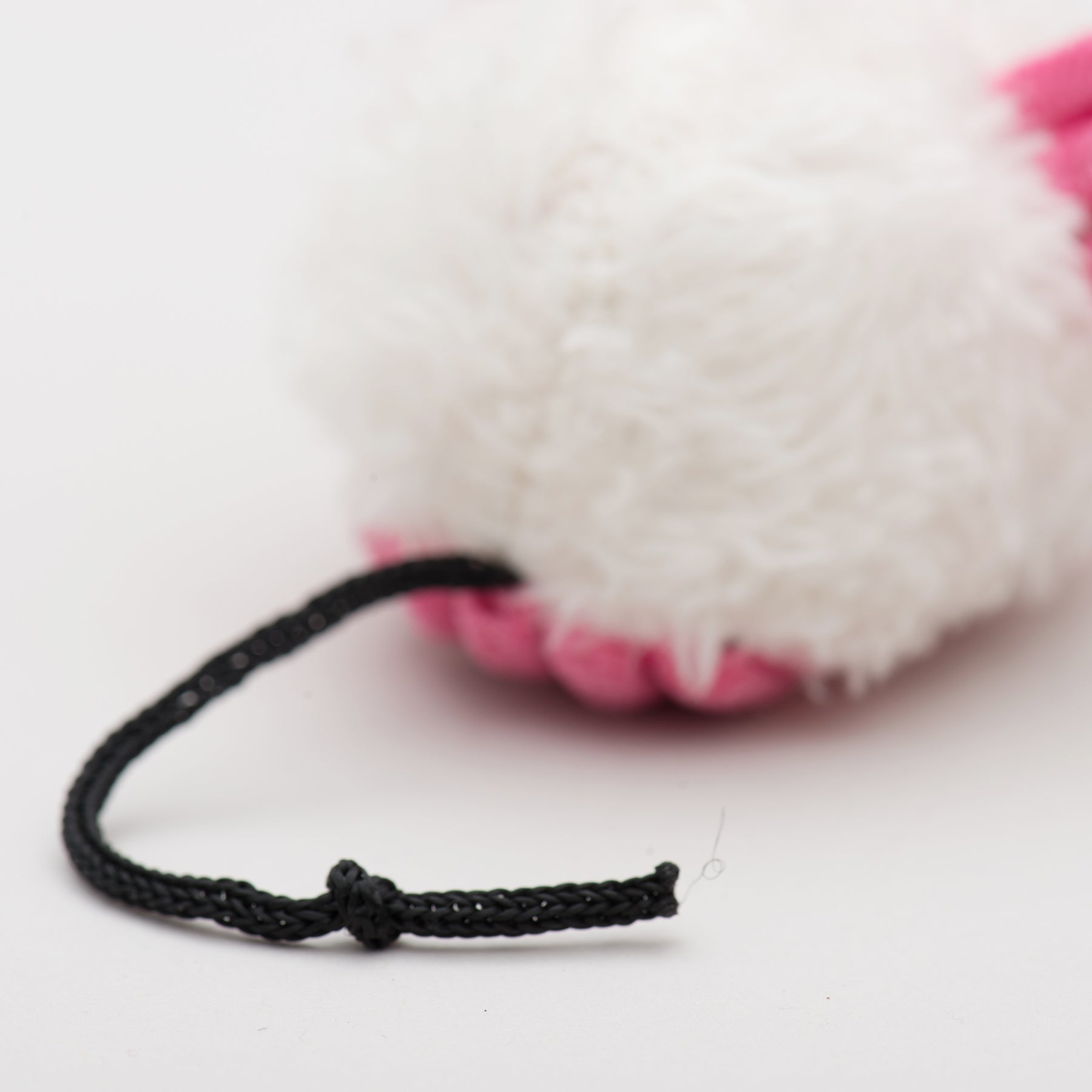 Close-up of a black cord tied to a white and pink plush toy on a light gray background.