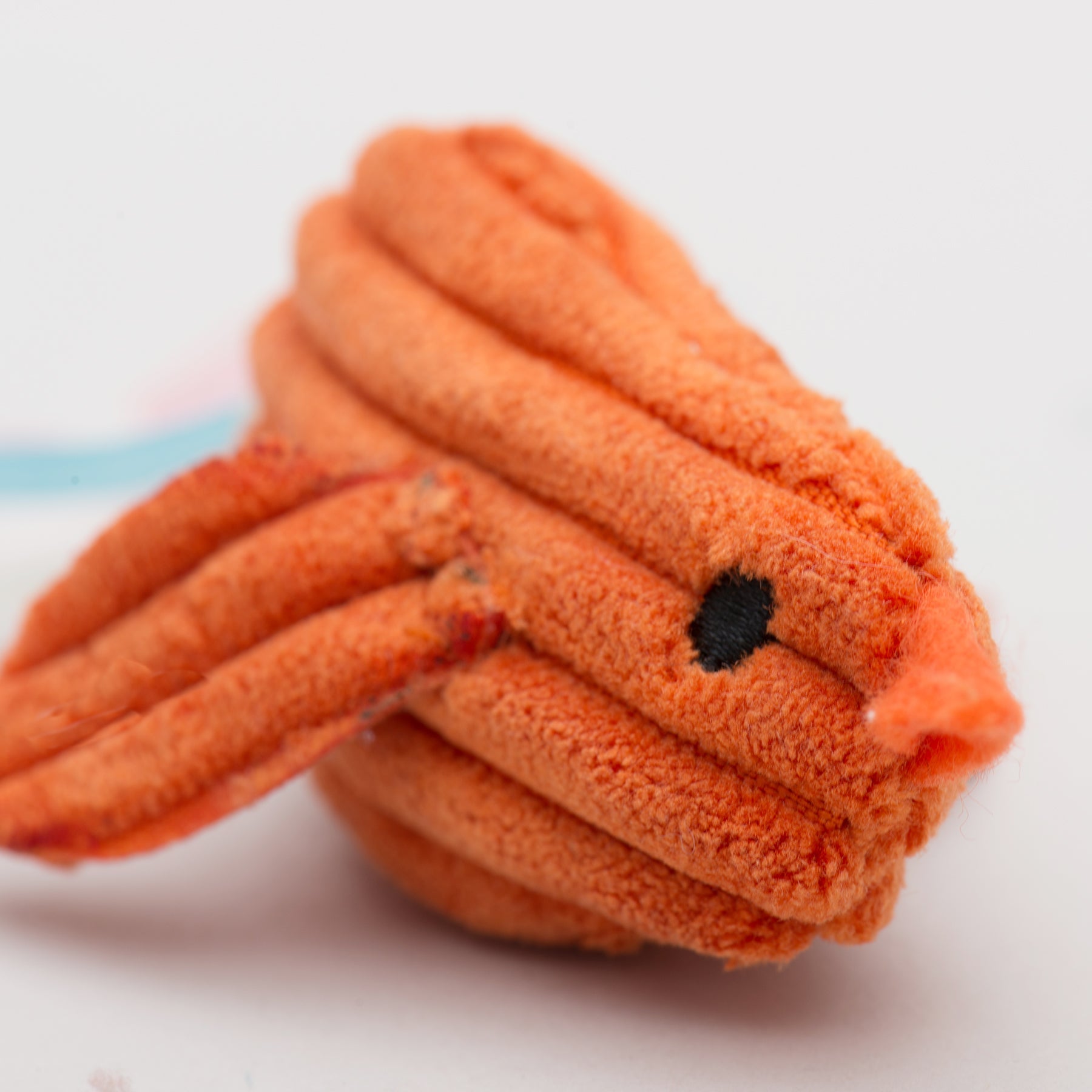 Close-up of an orange plush knotted cat toy on a white background.
