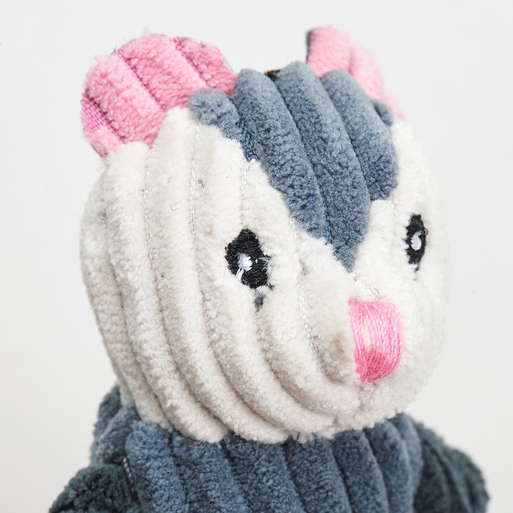 Close-up of a opossum plush toy with pink ears and a gray body on a white background.