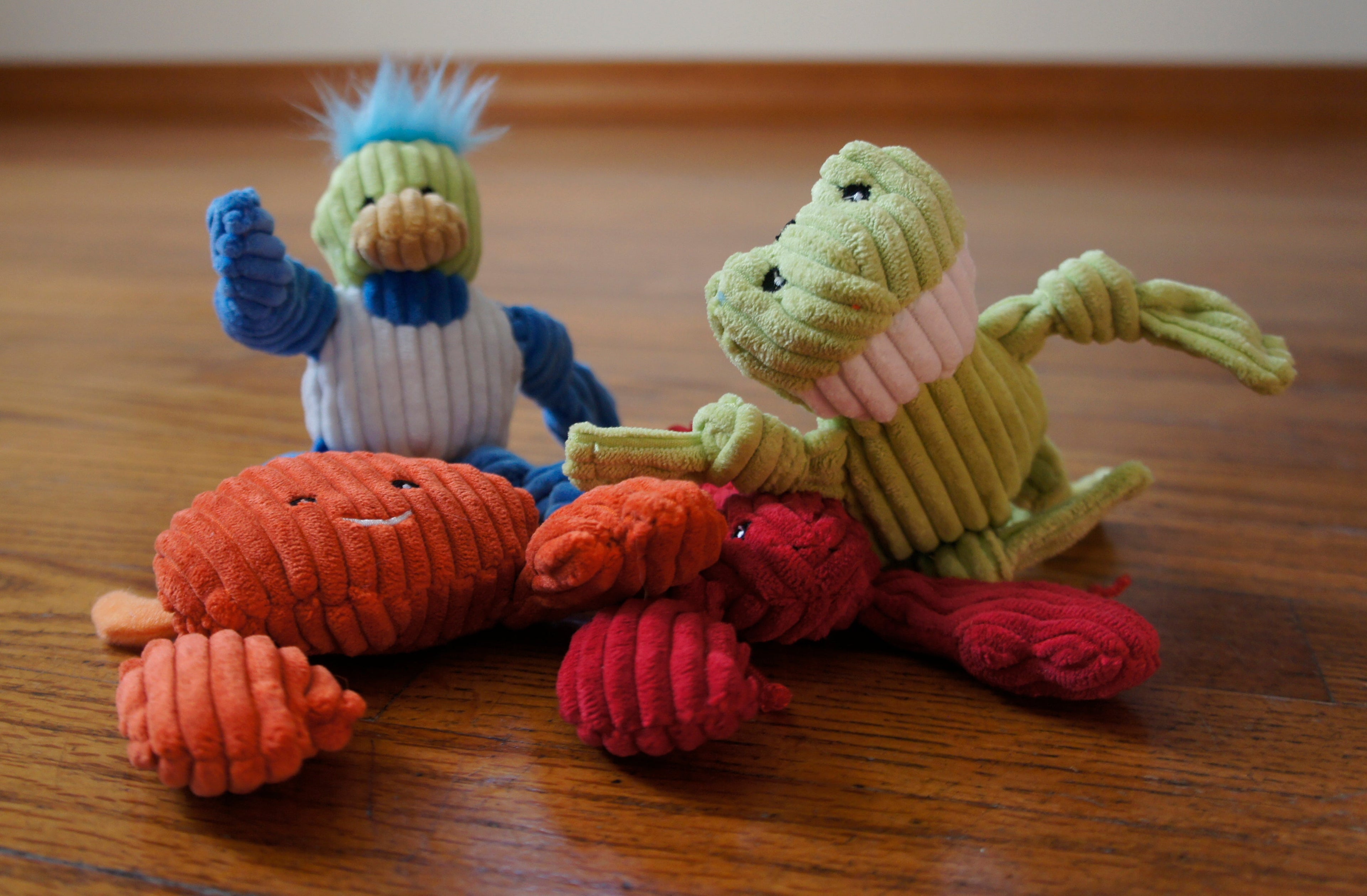 Colorful plush crab, lobster, bird, and frog cat toys on a wooden surface.